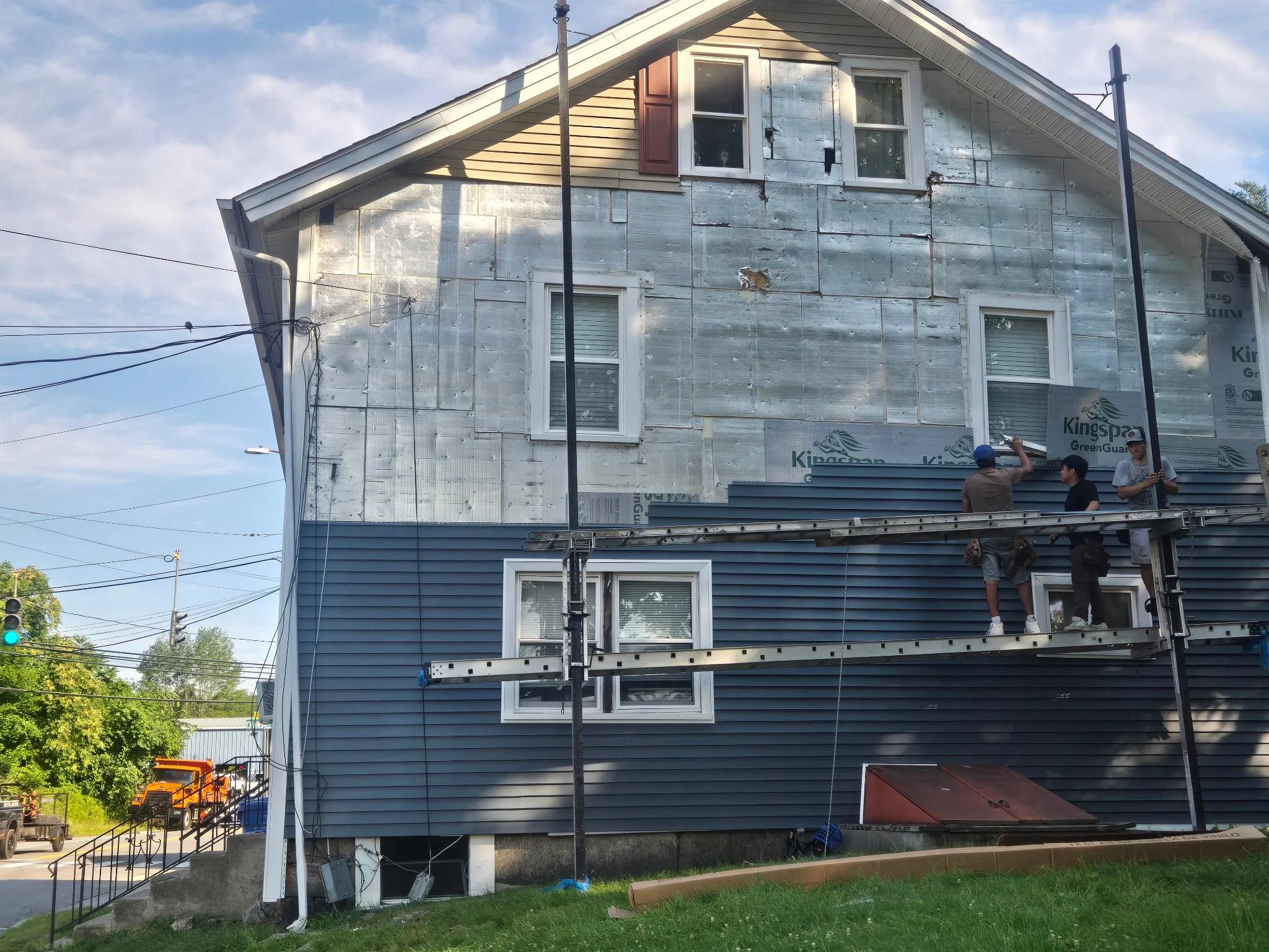 Two-story house with blue vinyl siding installation in progress, house wrap visible, new windows installed