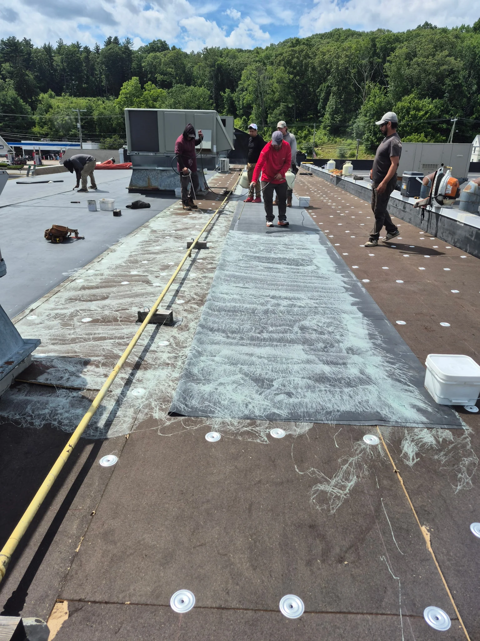Crew installing flat roof membrane with underlayment and fasteners on commercial building