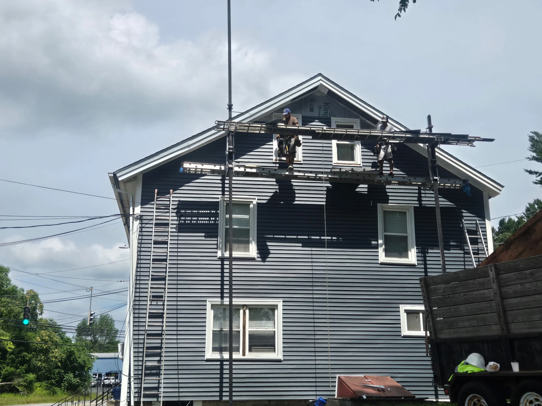 Two-story home with new dark gray vinyl siding, white trim, and soffit installation in progress