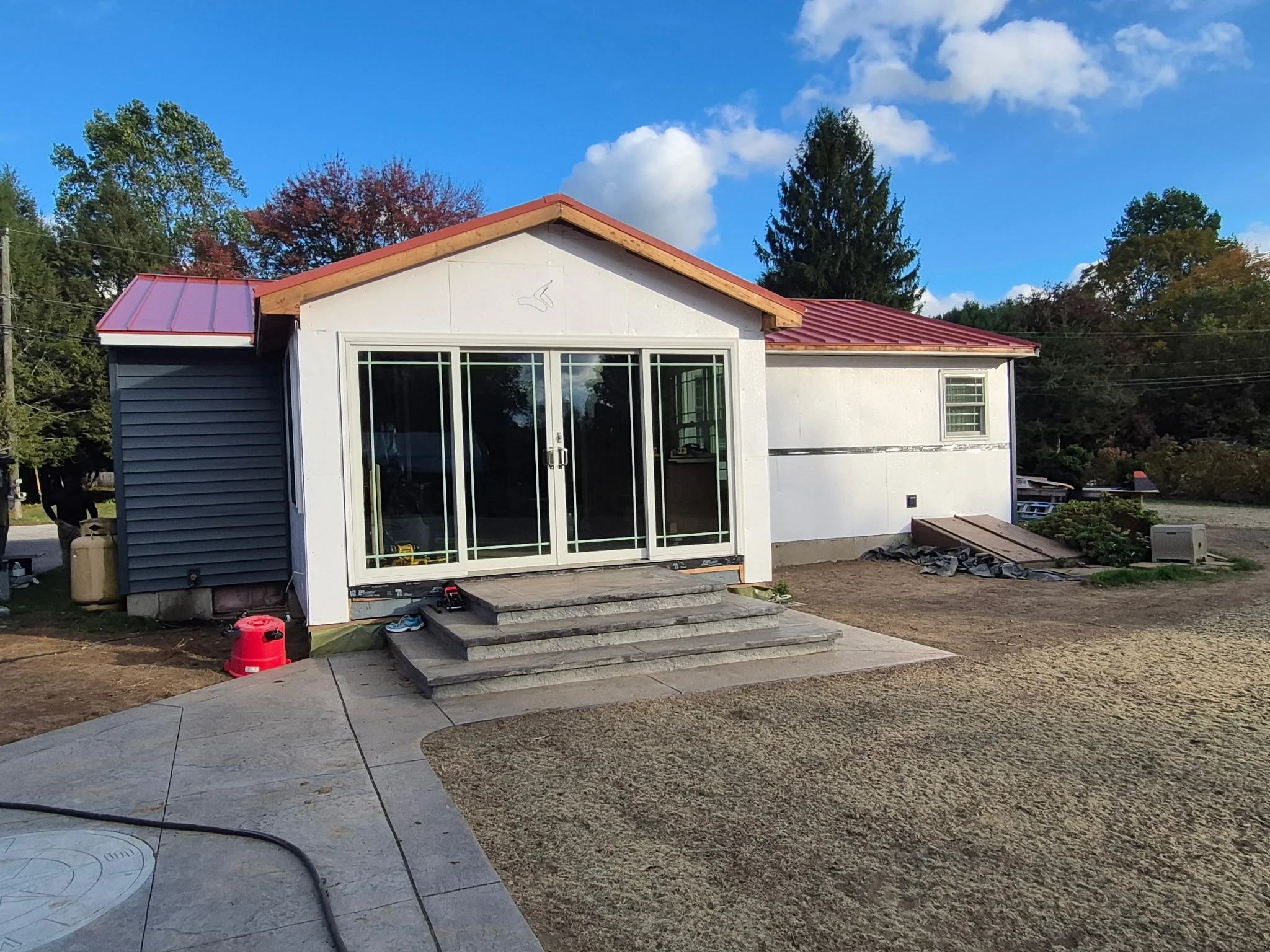 Standing seam metal roof with red panels, white siding, and multi-panel glass doors on modern home