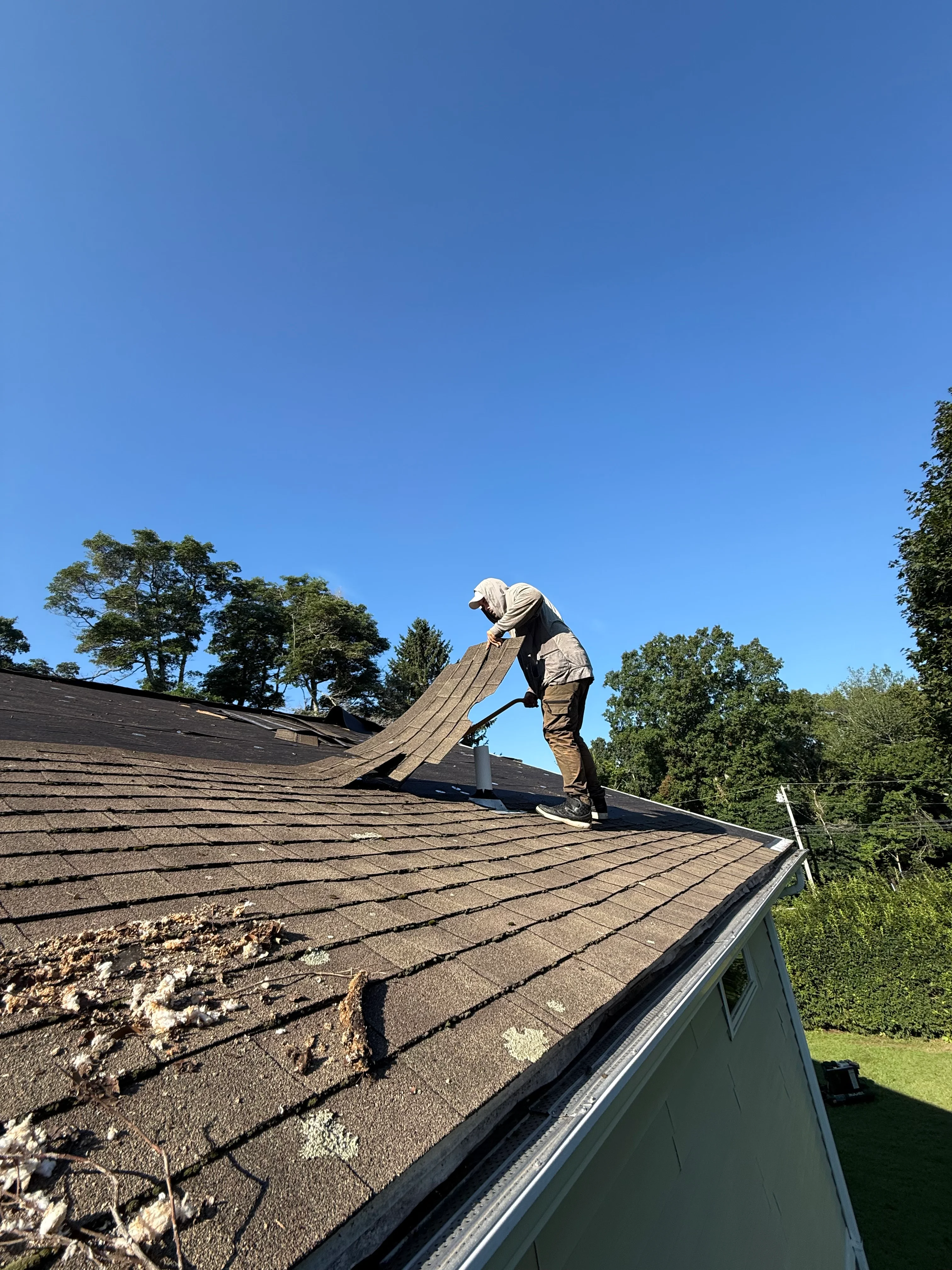 Roofer installing asphalt shingles on pitched residential roof with metal gutters