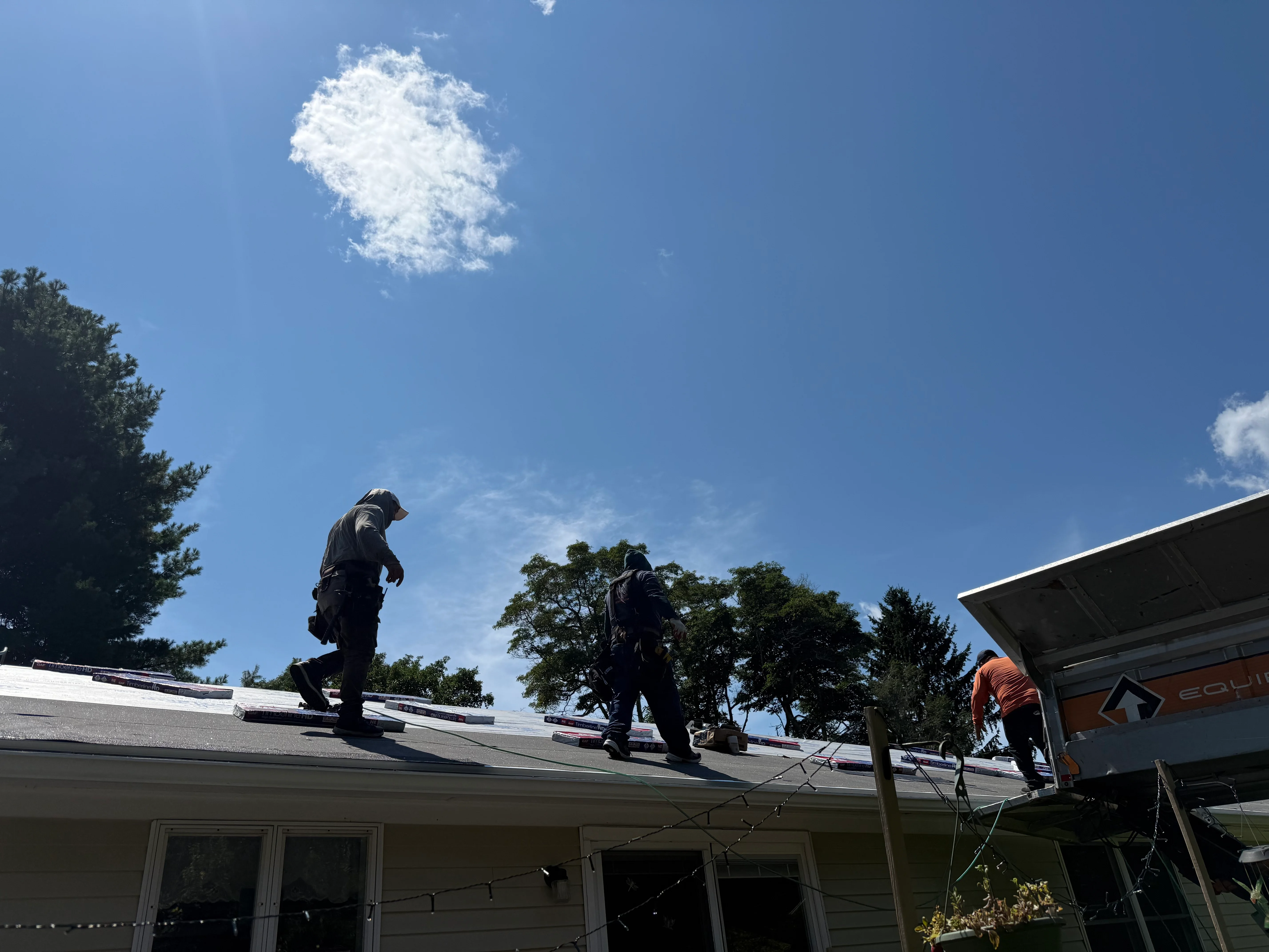Two roofers installing asphalt shingles on residential roof with white trim and gutters