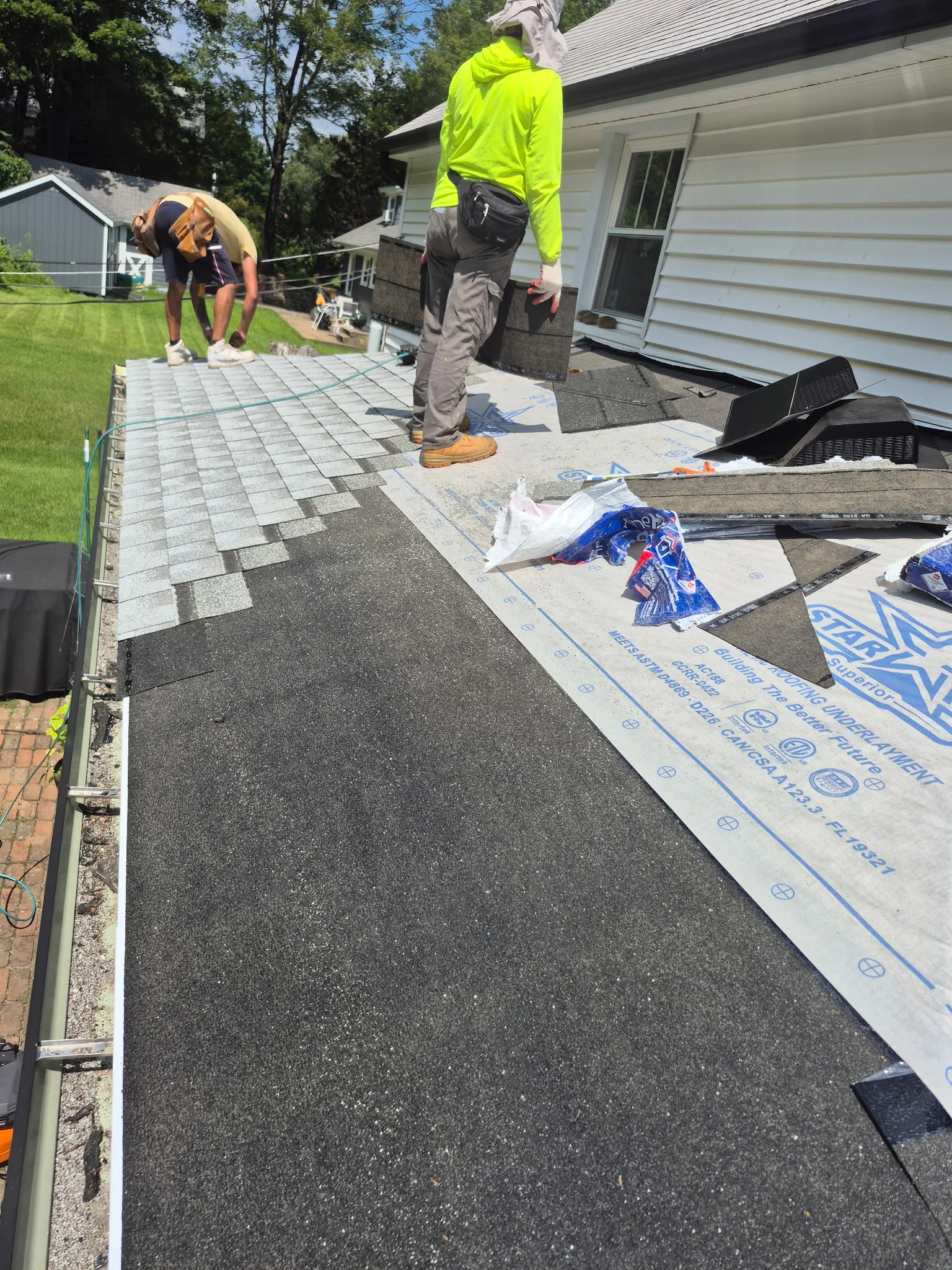 Roofers installing architectural shingles with underlayment and ice shield protection on residential home