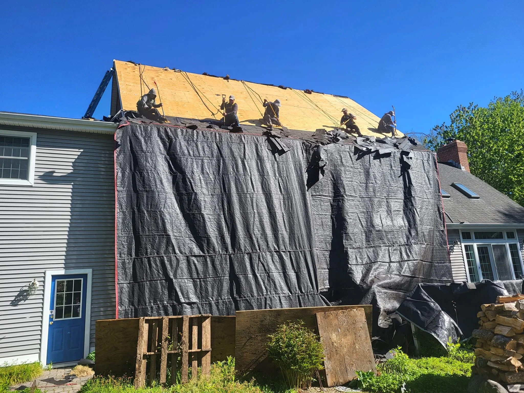 Roof replacement in progress with yellow underlayment, protective tarping, and crew working on pitched roof