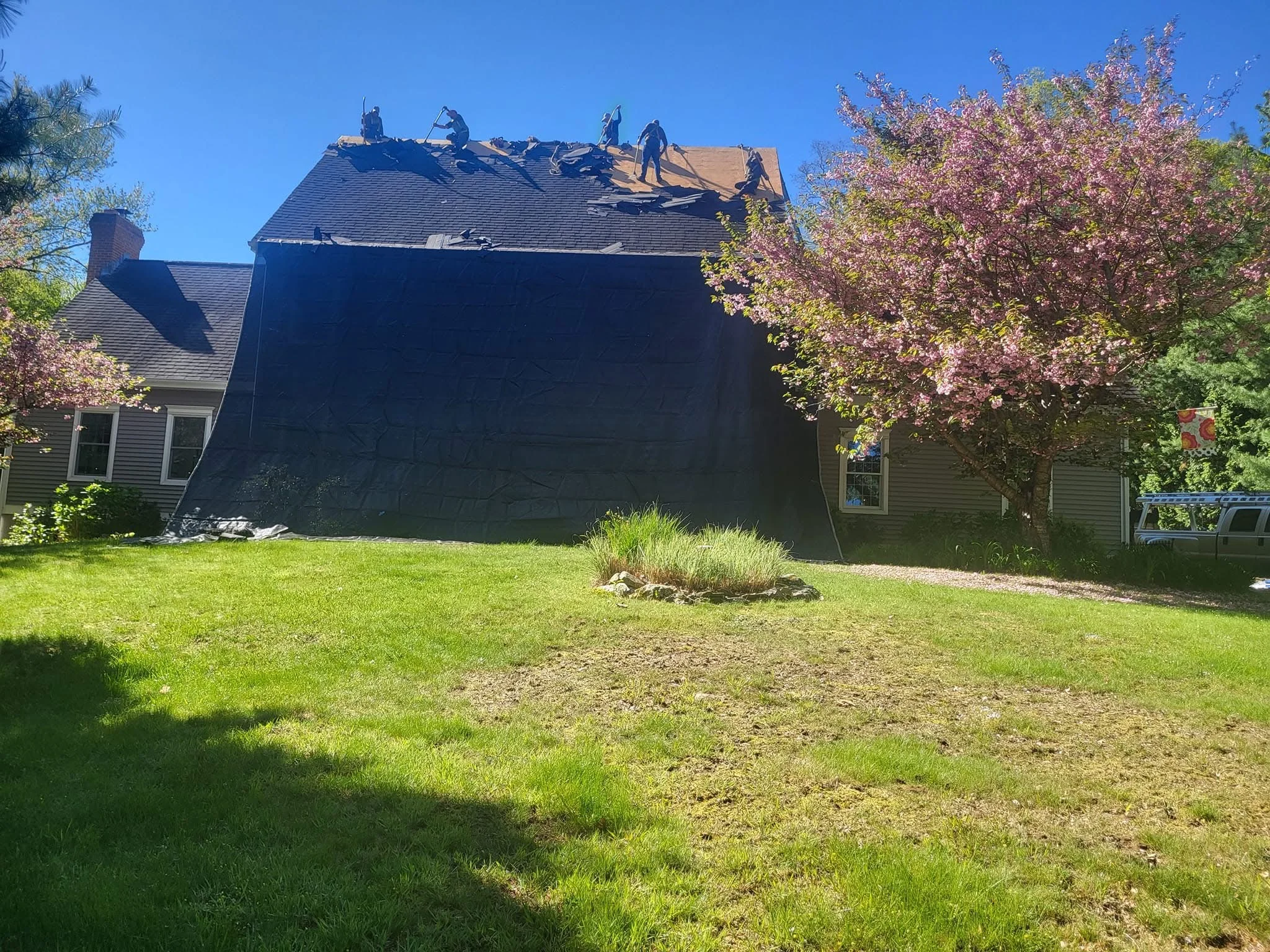 Residential roof replacement with dark gray architectural shingles and workers on pitched roof