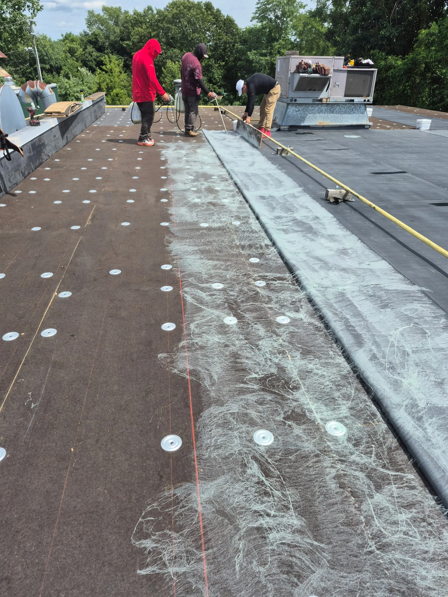 Crew installing flat roof membrane with fasteners and metal edge flashing on commercial building