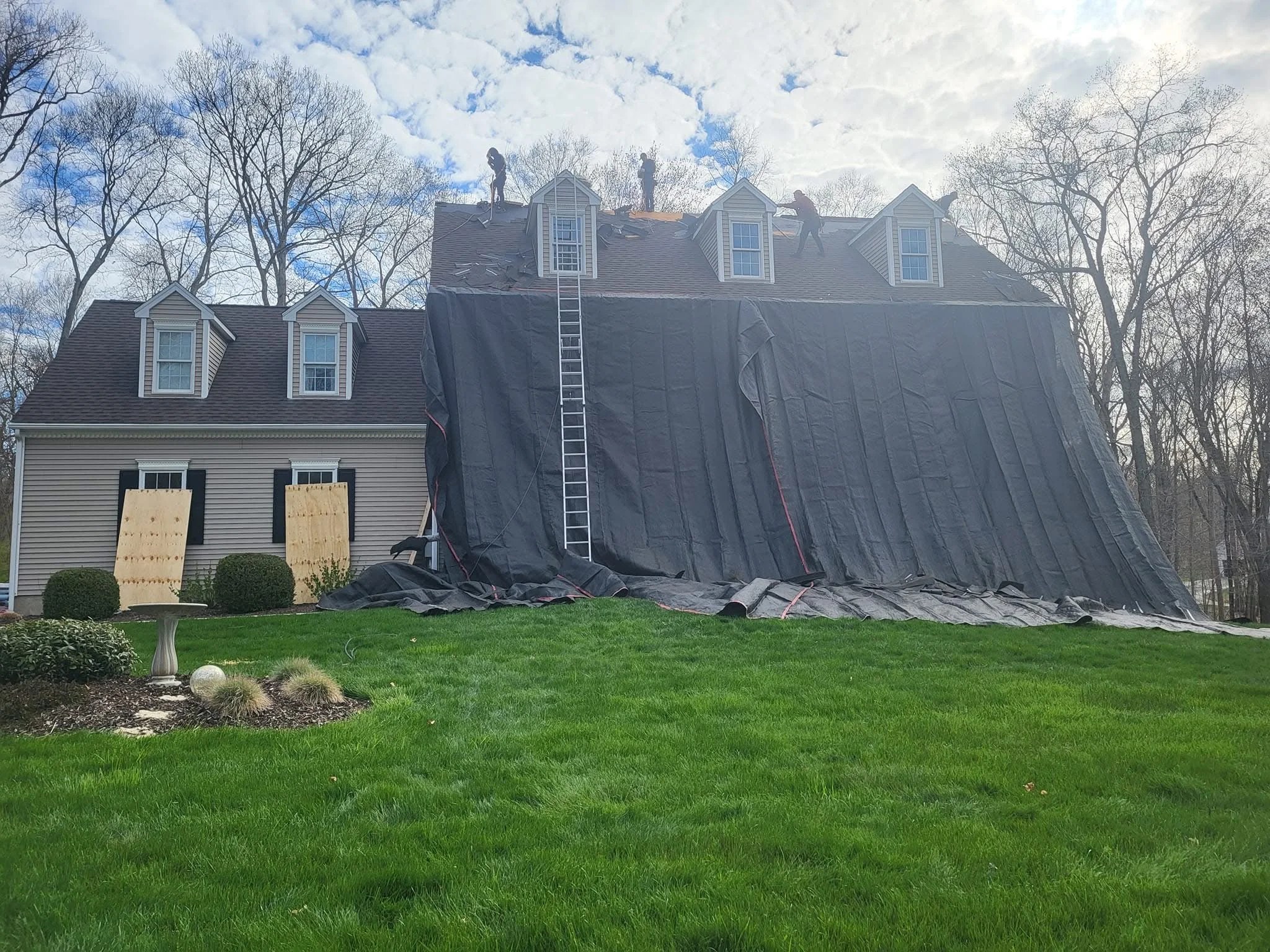 Two-story home with new asphalt shingle roof installation, protective tarping, and work staging