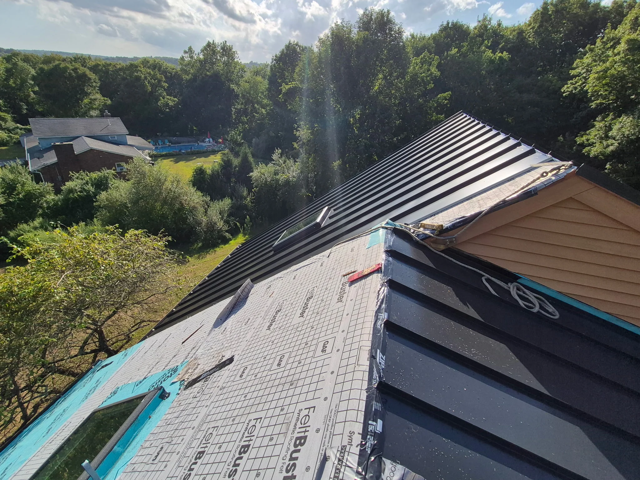 Black metal standing seam roof and architectural shingles installed on residential home with wooded backdrop