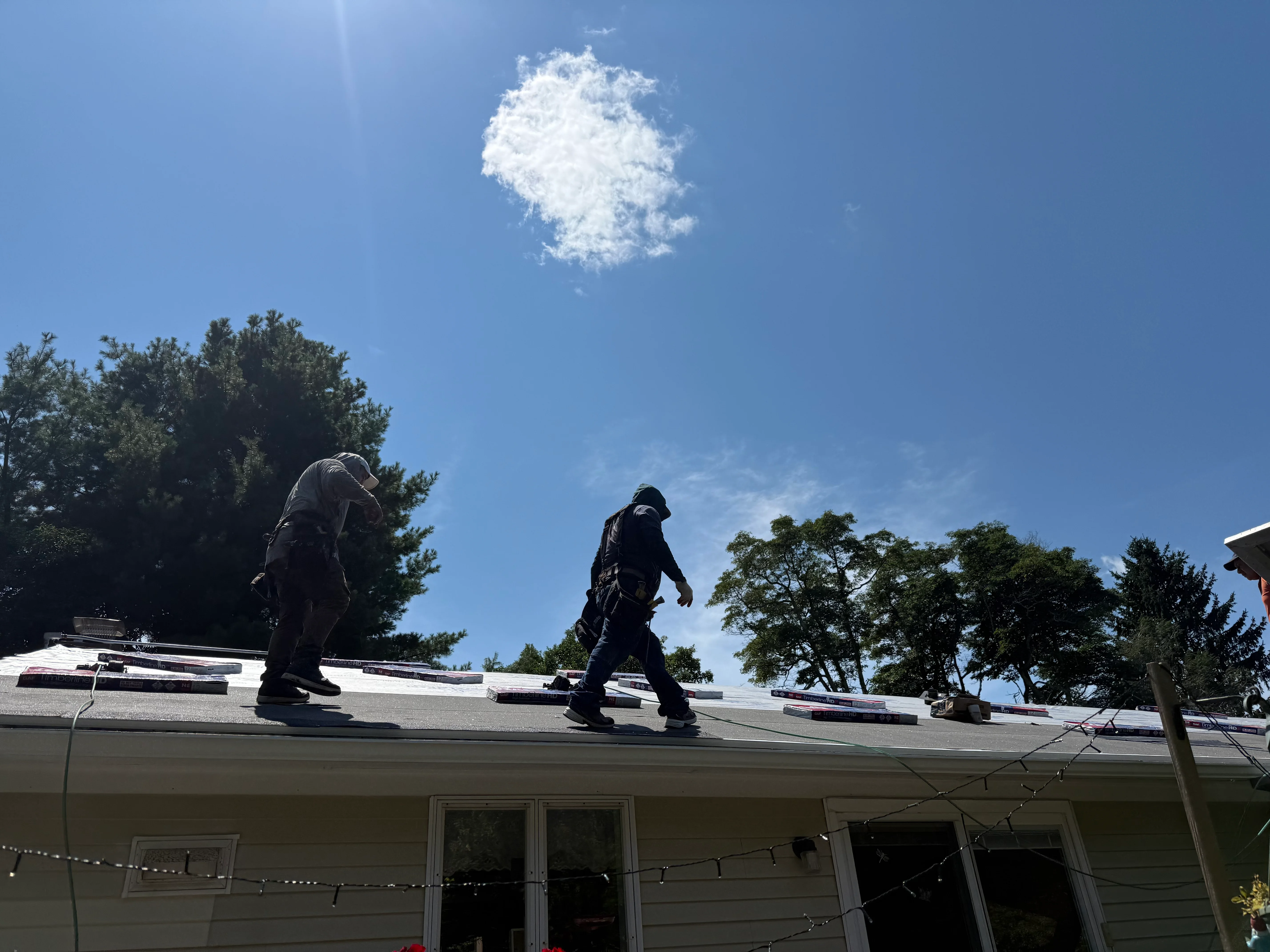 Two roofers installing asphalt shingles on residential roof with white and dark materials