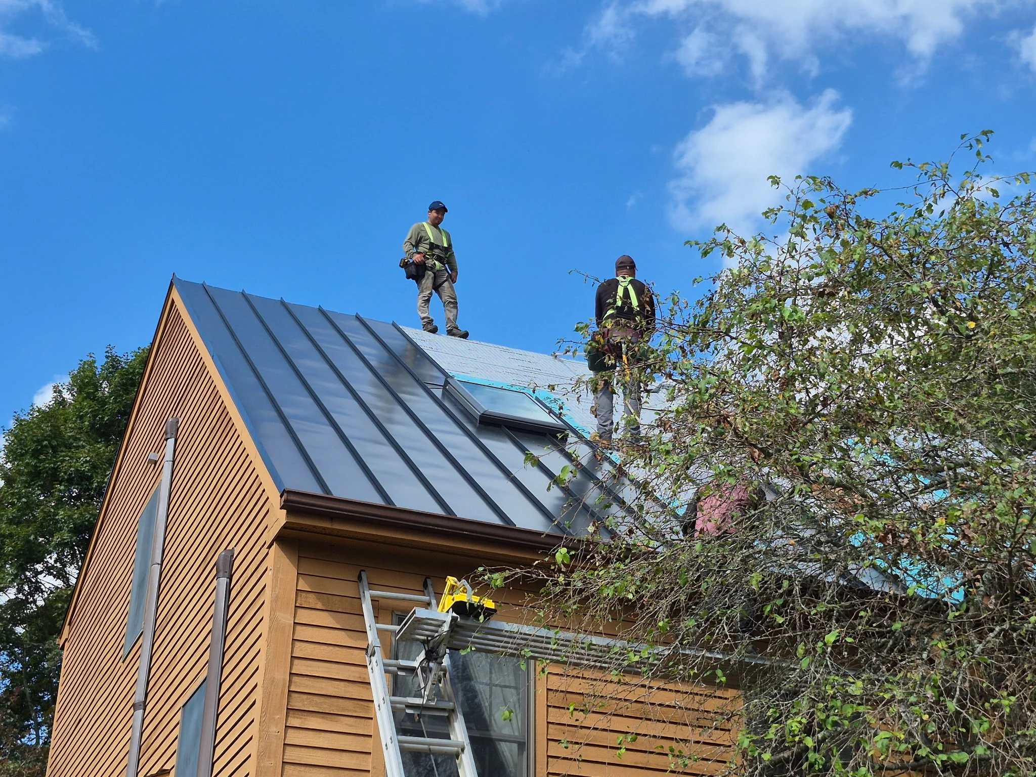 Standing seam metal roof installation with solar panels and two workers on pitched roof